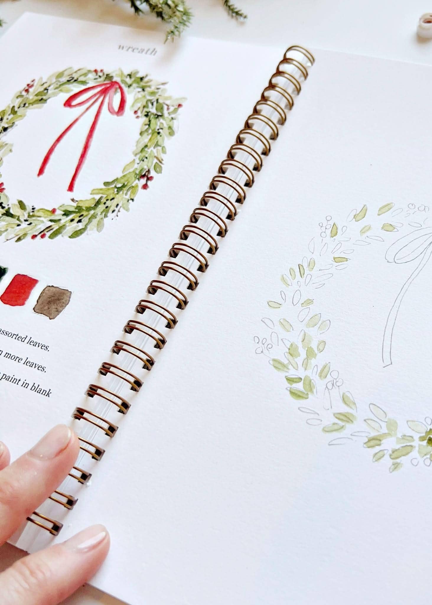 Image of someone painting a design of a wreath in the Christmas watercolor workbook.