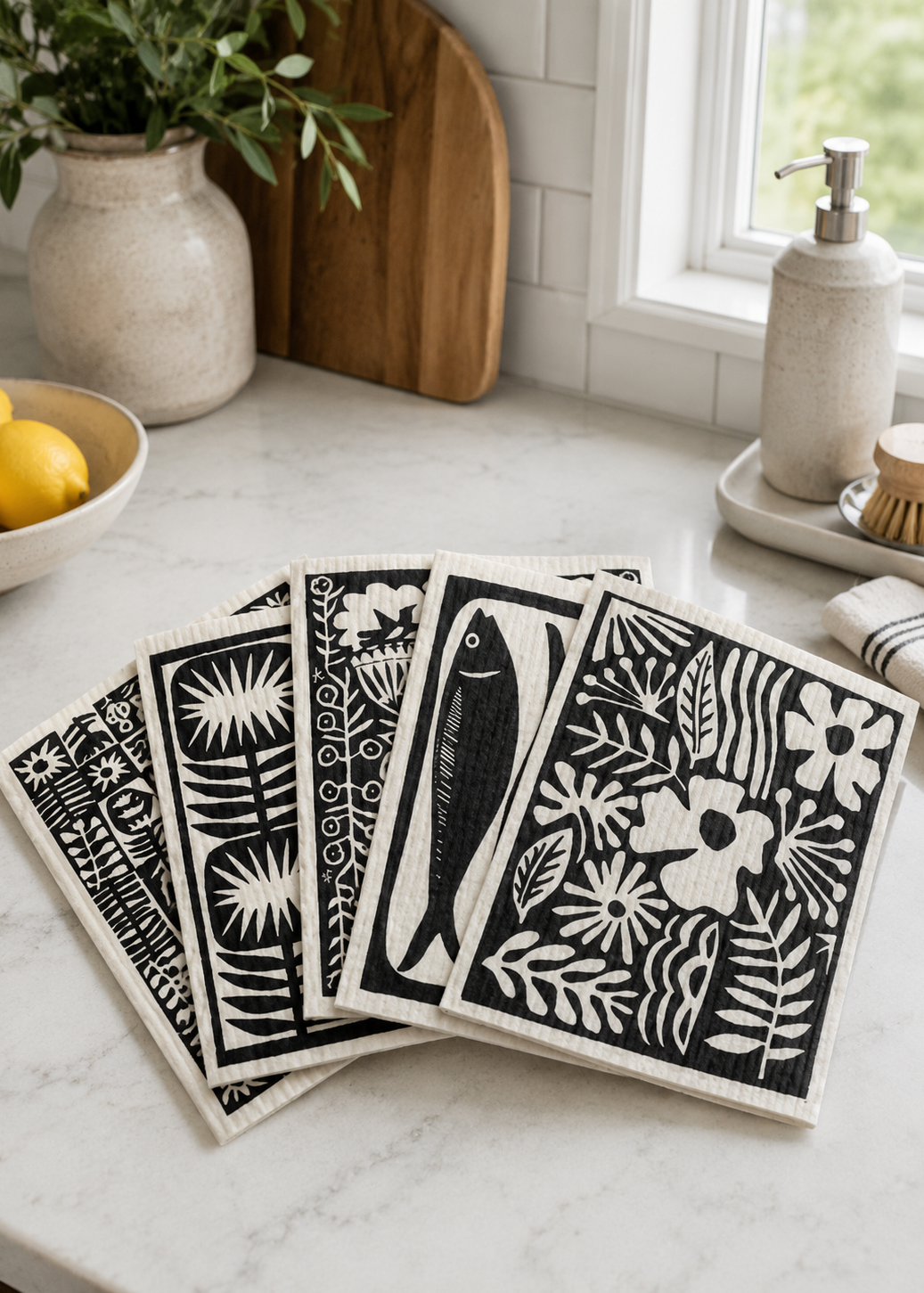All five coordinating Swedish dishcloths featuring original artwork by Jennifer Judd-McGee displayed together on a kitchen countertop.