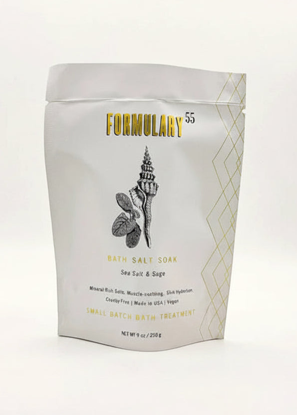 A stand-up pouch of Formulary 55 Bath Salt & Sage sea salt & sage bath salt soak, shown on a clean white background with a sprig of green leaves and pink salt crystals in front.