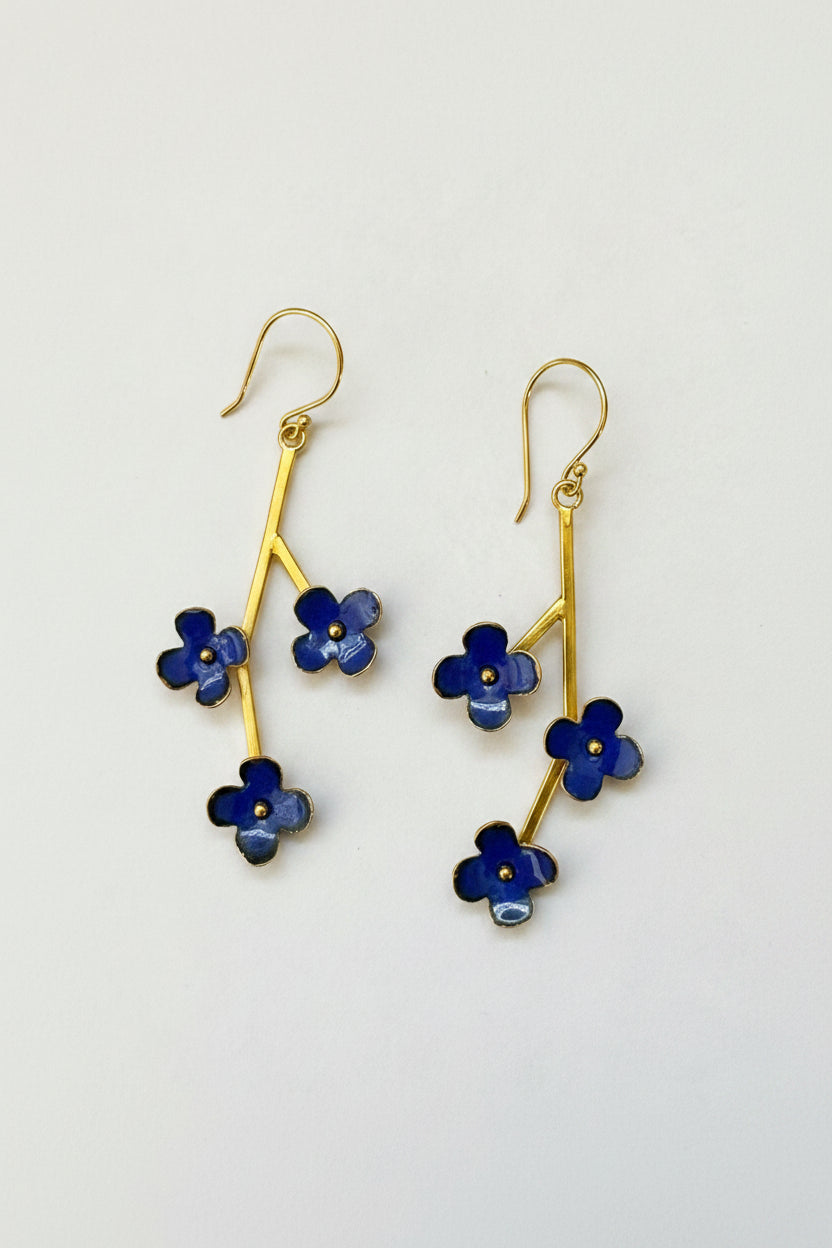 A pair of gold-tone dangle earrings with four-petal blue enamel flowers, photographed on a plain light gray background.
