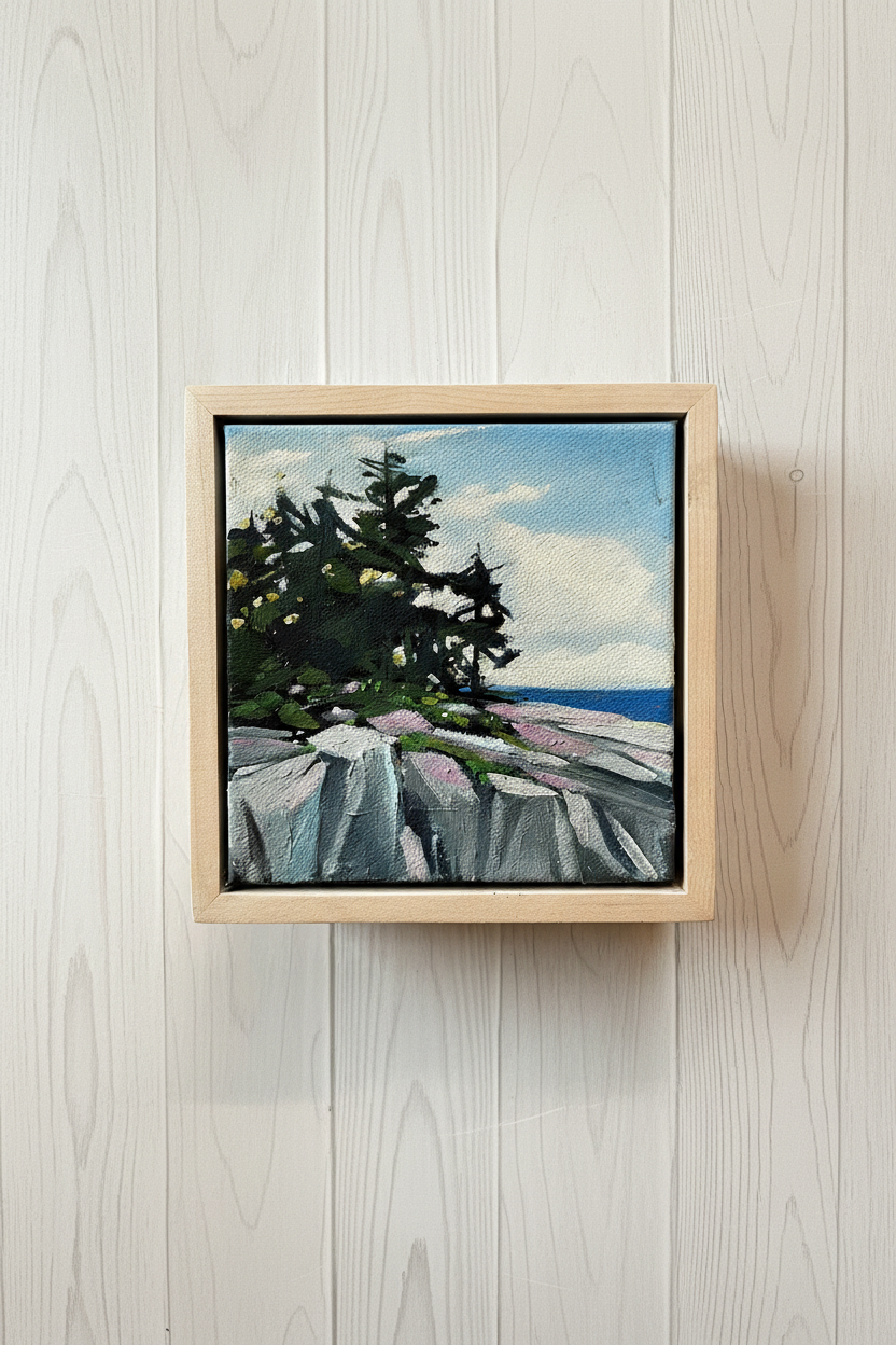 Framed painting of a coastal scene with trees and cliffs on a wooden wall.