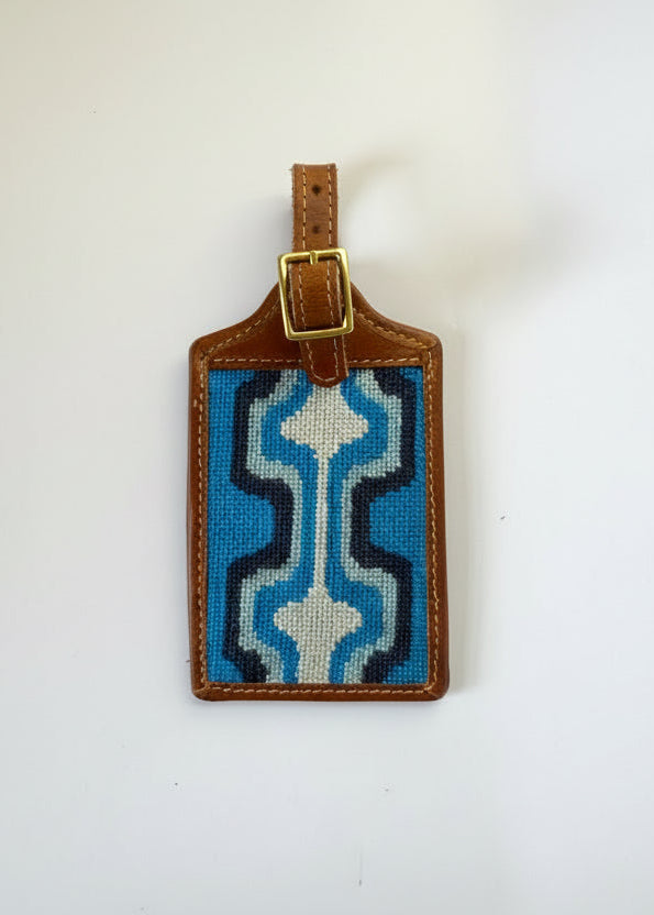 Luggage tag with blue and white pattern on a brown leather strap against a white background