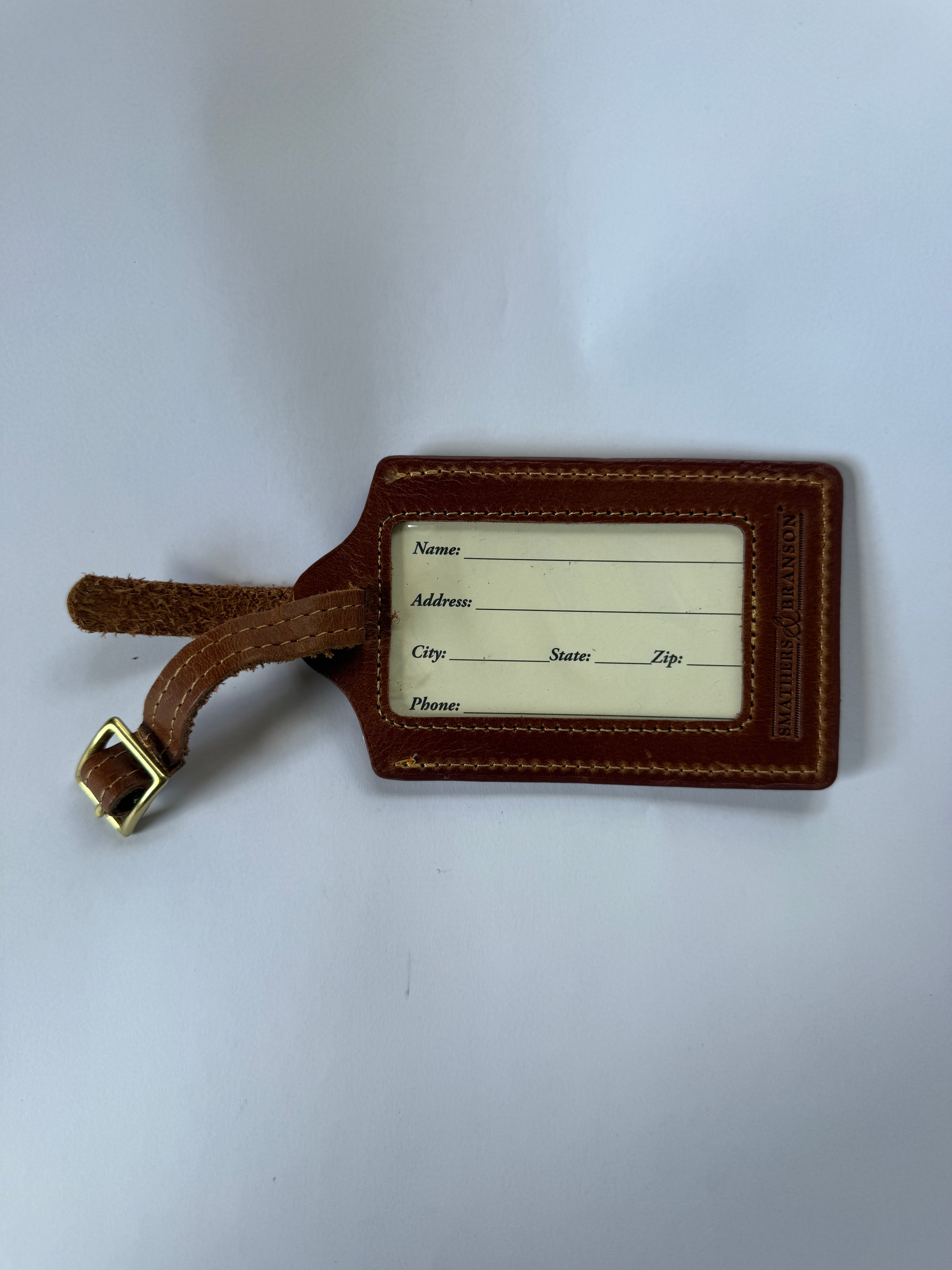 Brown leather luggage tag with a white label on a white background