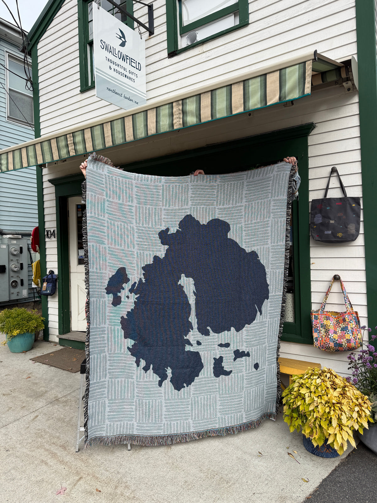 Mount Desert Island Woven Blanket by Jennifer Judd-McGee held up outside of the Swallowfield shop.
