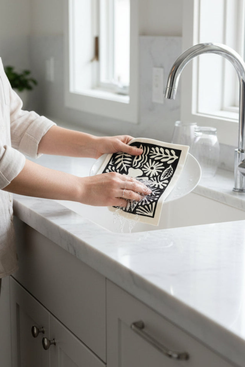 A woman washing dishes using a "Moonlight Garden" swedish dishcloth.