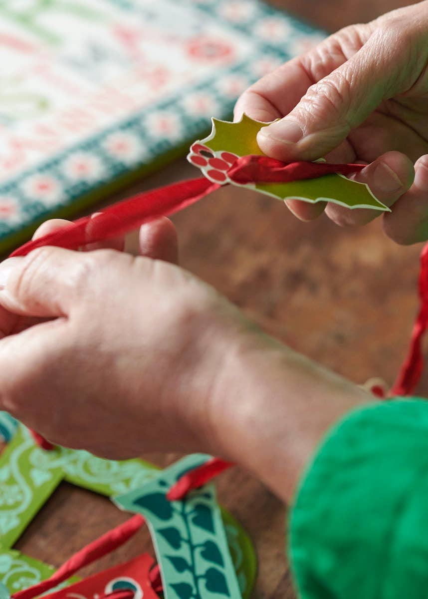 Image of a woman stringing the banner letters onto red silk ribbon.