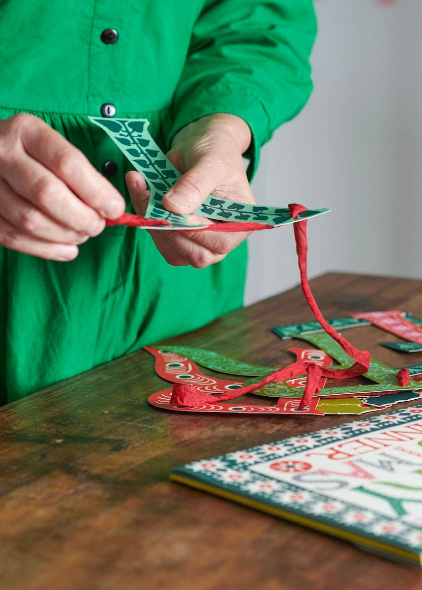 A photo of a woman stringing banner letters onto red silk ribbon.